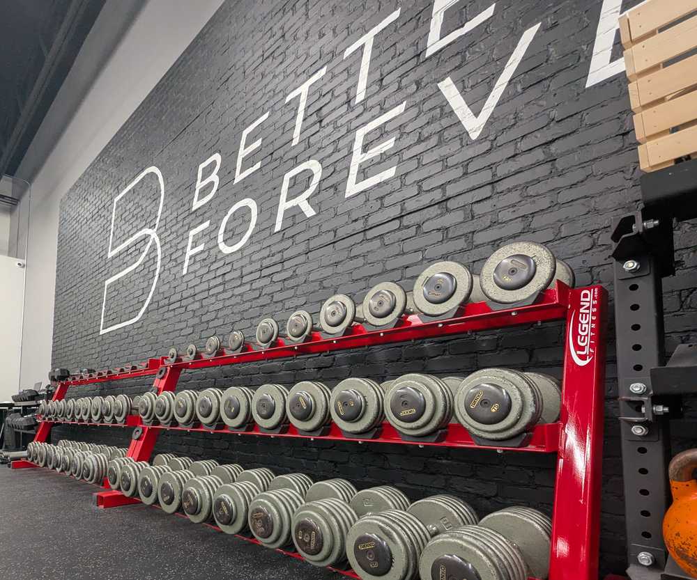Dumbbell racks beneath the Better Forever logo at the center